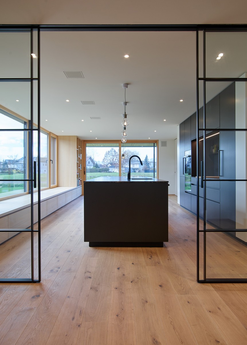 Eine großzügige Glasschiebetüre öffnet den Blick und führt fließend weiter in den Koch- und Essbereich, der sich unmittelbar zum Grünraum hin orientiert.