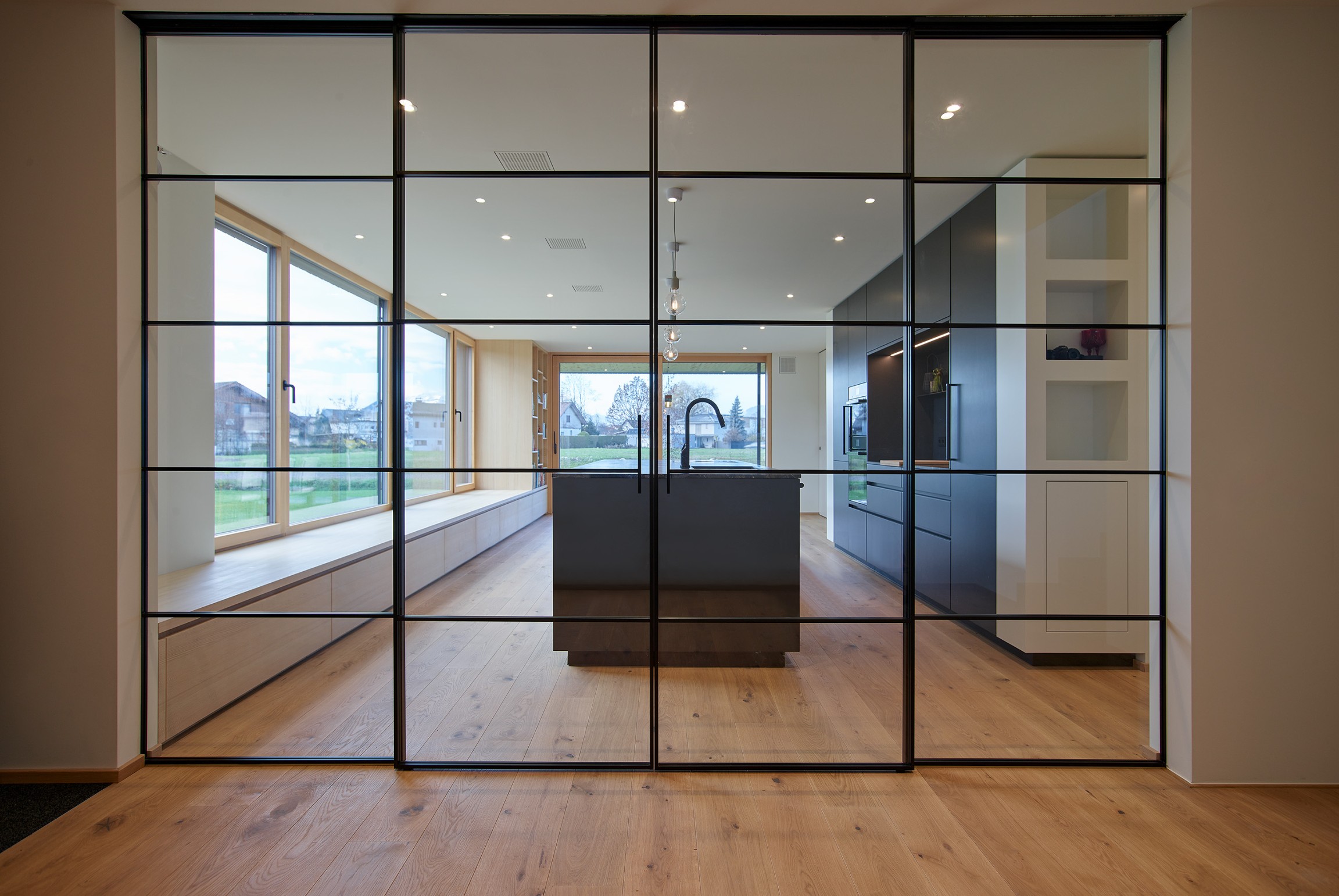 Eine großzügige Glasschiebetüre öffnet den Blick und führt fließend weiter in den Koch- und Essbereich, der sich unmittelbar zum Grünraum hin orientiert.