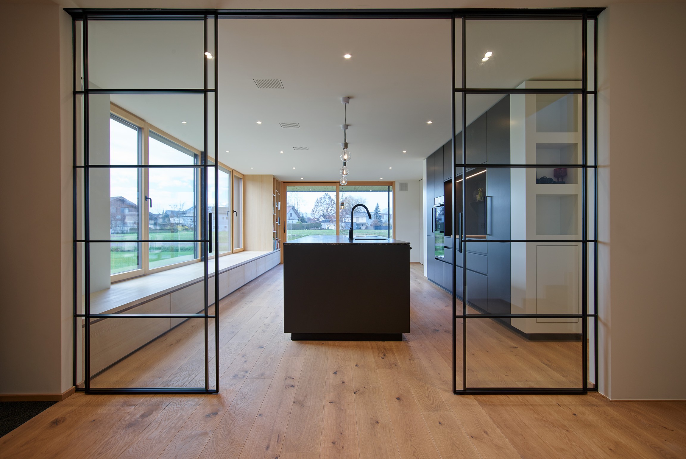 Eine großzügige Glasschiebetüre öffnet den Blick und führt fließend weiter in den Koch- und Essbereich, der sich unmittelbar zum Grünraum hin orientiert.